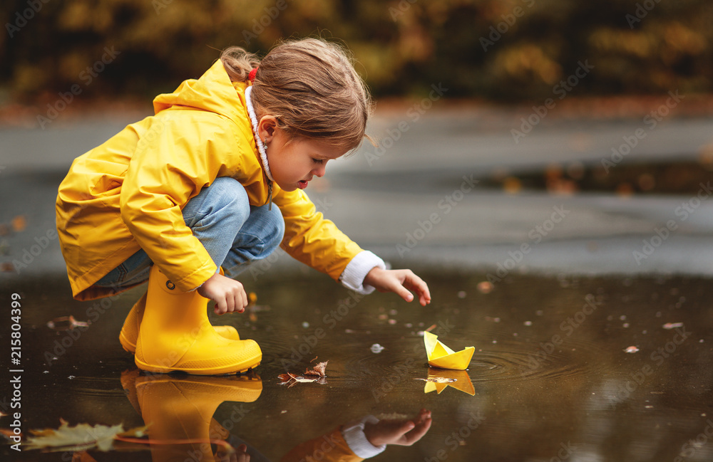 happy child girl with umbrella and paper boat in   puddle in   autumn on nature. - obrazy, fototapety, plakaty 