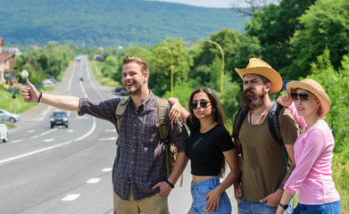 Wall Mural - Friends hitchhikers looking for transportation sunny day. Family weekend. Company friends travelers hitchhiking at edge road nature background. Begin great adventure in your life with hitchhiking