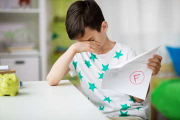 childhood, education and people concept - sad boy holding school test with f grade