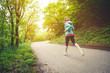 © yanik88 - Young fitness blonde woman in headphones running at morning caucasian forest trail in sun light. side view from behind