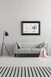 © Photographee.eu - Poster above grey sofa with pink blanket in living room interior with lamp and striped carpet. Real photo
