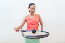 Close-up Of A Rubber Hollow Ball On The New Squash Racket Of A Fit Chinese Woman Standing Against White Wall 