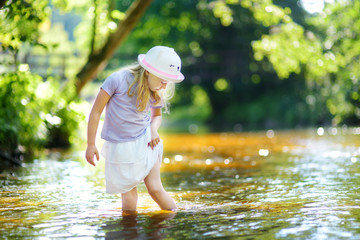 cute little girl playing by a river on hot summer day. adorable child having fun outdoors during sum