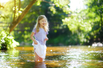 Wall Mural - Cute little girl playing by a river on hot summer day. Adorable child having fun outdoors during summer vacations.