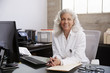 © Monkey Business - Senior female doctor sitting at desk in an office, portrait