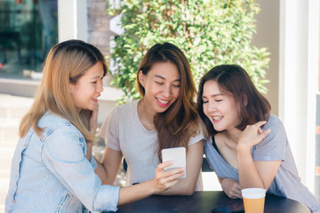 Cheerful asian young women sitting in cafe drinking coffee with friends and talking together. Attractive asian woman enjoying coffee while using smartphone for talking, reading and texting.