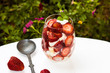 Strawberres and cream dessert in the glass bowl and spoon  on a the white table in the garden