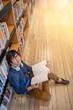 © zephyr_p - Young Asian man university student with glasses and headphones reading book sitting by bookshelf in public library, education research and self learning in university life concepts