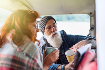 Old hipster couple sitting in a van and looking at a road map 