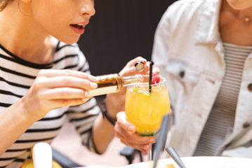 Wall Mural - Pouring whisky. Young woman wearing white and black shirt pouring some whisky to cocktail