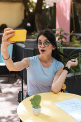 Wall Mural - Funny selfie. Modern woman wearing glasses making funny face while sending selfie her friend