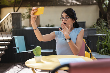 Wall Mural - Video chat. Dark-haired beautiful woman feeling extremely surprised during video chat with friend