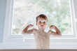© jakob/Stocksy - Cute young boy standing up and flexing his muscle in a bath tub