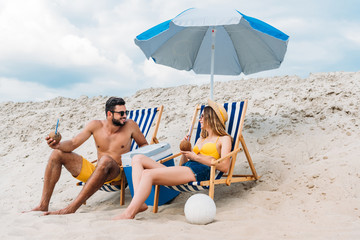 beautiful young couple with coconut cocktails relaxing in sun loungers on sandy beach