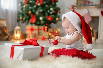 Wall Mural - Cute baby in Santa hat playing with jingle bell at home. Christmas celebration