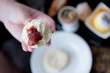 Hand of Asian woman hold a half split freshly baked scone spread with clotted cream first, and topped with strawberry jam, Devon or Devonshire way, during afternoon tea or high tea. Natural lighting.