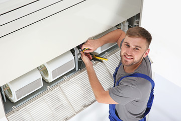 Wall Mural - Young male technician repairing air conditioner indoors