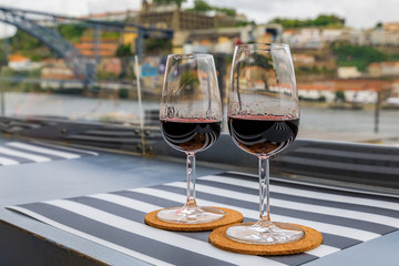 Wall Mural - Glasses of port wine at an outdoor restaurant with the Douro river and Dom Luis I bridge blurred in the background in Porto, Portugal