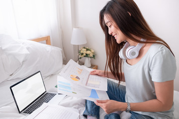 Poster - Asian woman freelancer working on paperwork on bed with laptop in bedroom.work at home concept.
