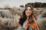 Fototapeta Boho - Back side of boho woman with windy hair in the desert nature, turning her head and smiling .  Artistic photo of young hipster traveler girl in gypsy look, in Coachella Valley in a desert vall