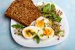 Zdrowe śniadanie: Jajka gotowane na twardo, świeże kiełki, rukola i kromka pełnoziarnistego chleba  na niebieskim tle, 