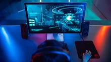 High-angle Shot Of The Professional Gamer Playing In First-Person Shooter Online Video Game On His Personal Computer. Room Lit By Neon Lamps In Retro Arcade Style.