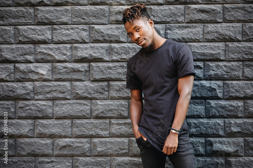 Cuadros en Lienzo Handsome african american man in blank black t-shirt standing against brick wall