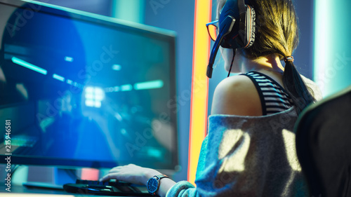 Shot of the Beautiful Pro Gamer Girl Playing in FPS Video Game on Her Personal Computer, Casual Cute Geek wearing Glasses and Headset. Neon Room. Playing Online Games.