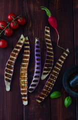 Long and slim grilled finger eggplant with basil leaves, tomatoes and radish on wooden background. Grilled vegetables on dark background. Healthy vegan food.