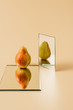 one ripe pear reflecting in two mirrors on beige table