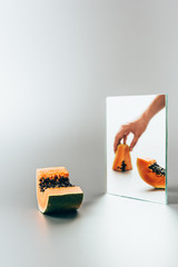 Wall Mural - cropped image of woman holding yellow papaya reflecting in mirror on white table