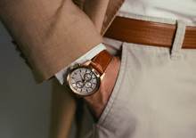 Closeup Fashion Image Of Luxury Watch On Wrist Of Man.body Detail Of A Business Man.Man's Hand In Brown Pants Pocket Closeup At White Background.Man Wearing Brown Jacket And White Shirt.Toned.