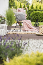 Cozy Pillow With Pattern And A Pink Blanket On A Garden Chair Outside On A Wooden Terrace With Rugs And Plants
