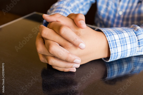 Fotografia, Obraz Clasped hands resting on dark reflective table top, blue plaid shirt sleeves