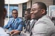 © xartproduction - Group of happy diverse male business afro - american people team in formal gathered around laptop computer in bright office against the background of a glass building