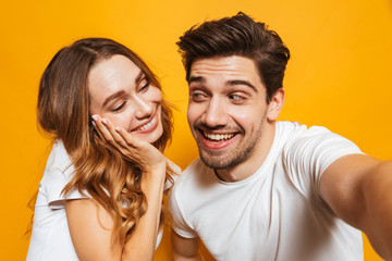 Canvas Print - Portrait of excited smiling couple man and woman taking selfie photo together, isolated over yellow background