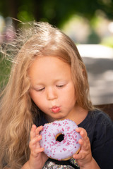 beautiful cute little girl sitting on a chair and eating a purple donut