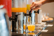 © Take Production - close up hand pulling down the lever of juice dispenser for fresh orange juice.