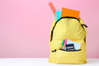 Yellow backpack with school supplies on pink background