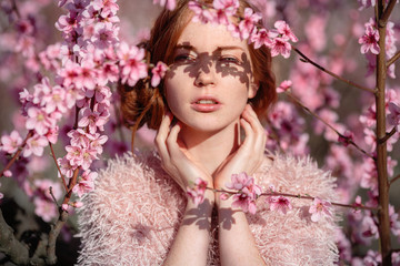 Beautiful young girl with red hair in a gentle peach garden, which blossomed.