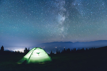 green tent lighted from the inside by a flashlight against the backdrop of an incredible starry sky.