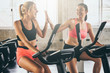 © ronnarong - Attractive young women working out together on exercise bike at the gym.