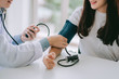 © chompoo - Doctor using sphygmomanometer with stethoscope checking blood pressure to a patient in the hospital.