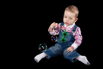 Little boy blowing soap bubble on black background