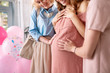 © zinkevych - Pregnant tummy. Two excited women touching pregnant tummy of their friend while celebrating baby shower