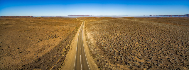 Rural road passing through dry land with scarce vegetation at sunrise  - wide aerial panorama