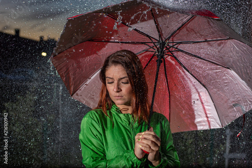 Young Woman In Green Raincoat In Rain With Red Umbrella At