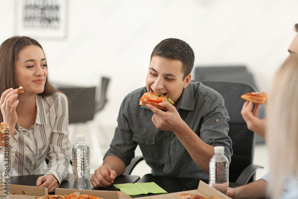 Young people eating pizza at table in office