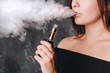 Close-up view of charming young woman with short hair smoking an e-cigarette, cloud of vapor.