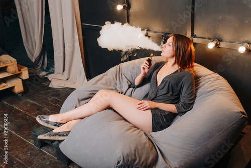 Lovely Attractive Girl Exhaling Vapor While Smoking An Electronic Cigarette Spending Leisure Time While Resting On Soft Pouf Sitting In The Design Room Stock Photo Adobe Stock